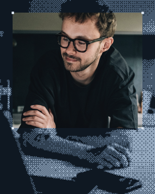 A man with glasses, arms folded at his desk.